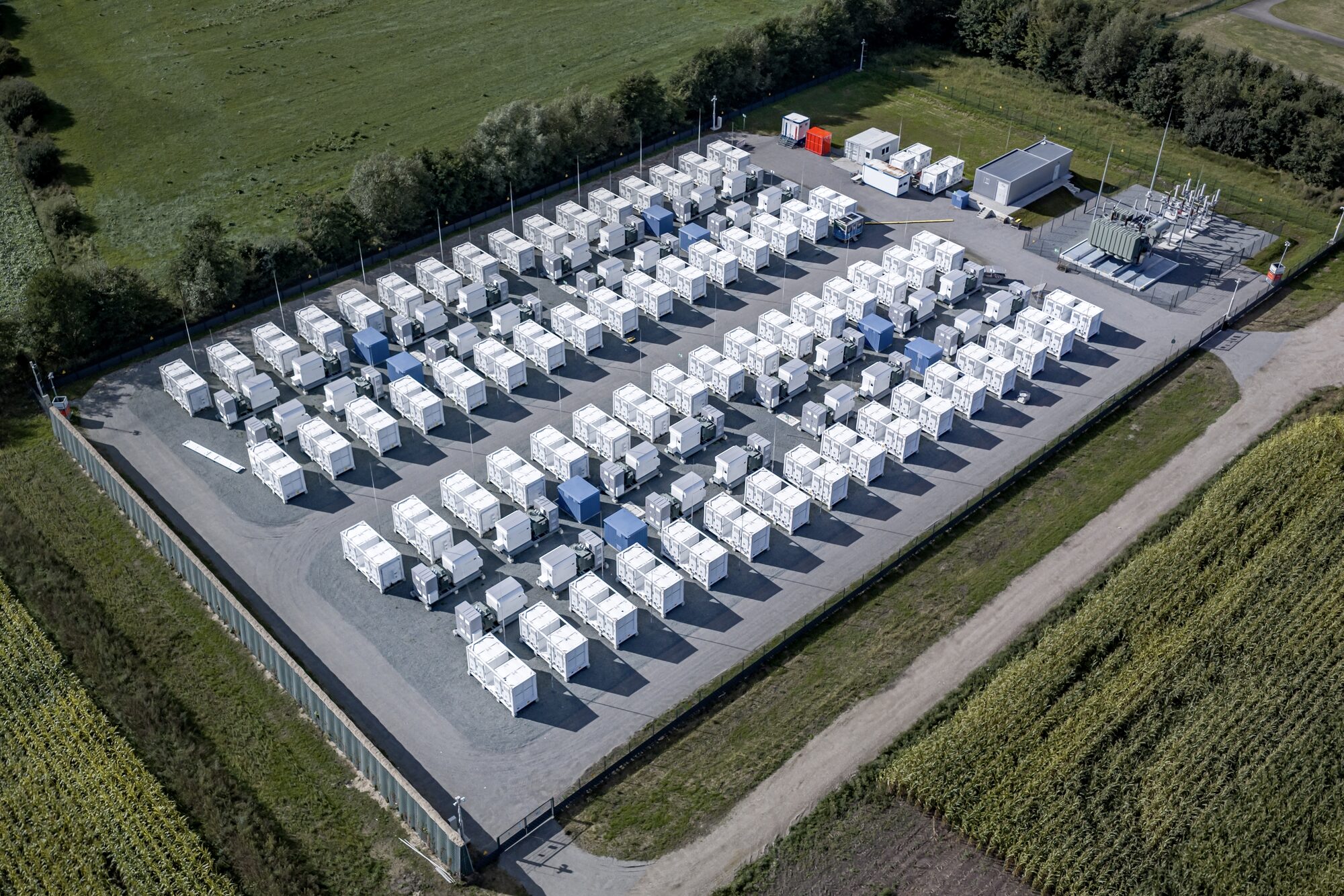 Aerial view of rows of battery containers beside a substation in open farmland